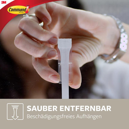 O persoană îndepărtează un cârlig Command™ mat negru de dimensiuni medii (17034B, 1 cârlig, 2 benzi) de la 3M Deutschland GmbH de pe perete. Textul german „Îndepărtare curată, agățare fără deteriorare” promovează îndepărtarea curată și agățarea fără deteriorare.